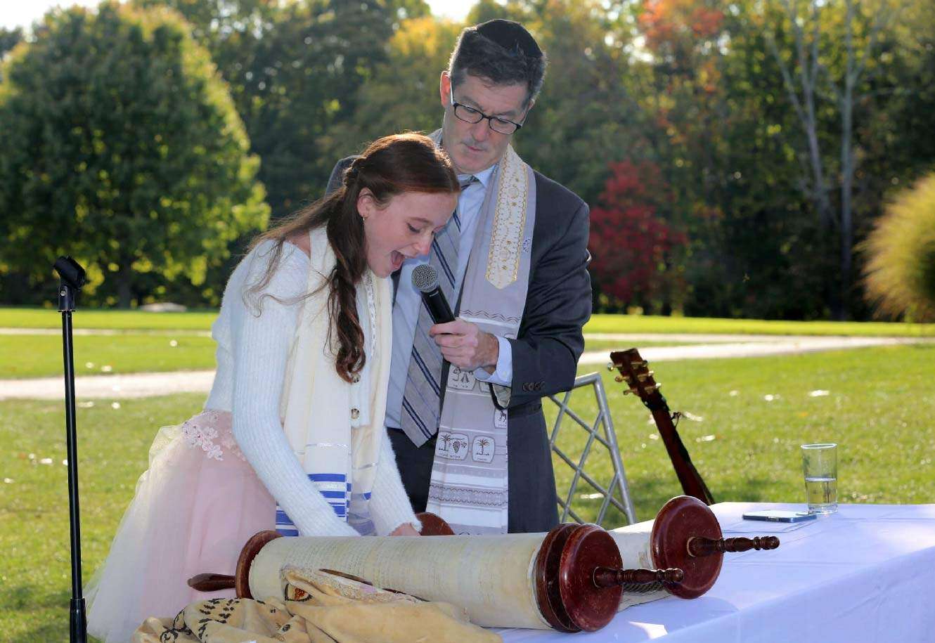 Rabbi Ron Broden holding a microphone for a young girl at her bat mitzvah.