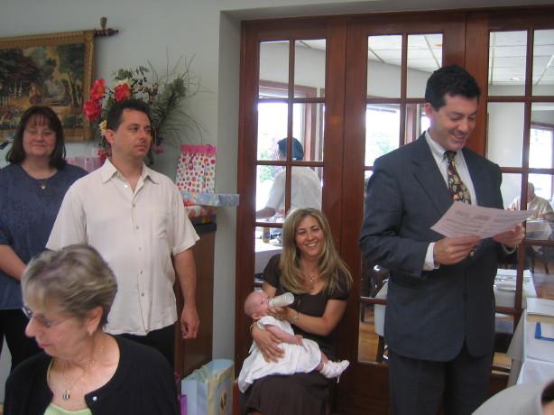 Rabbi Cantor Ron Broden holds a baby naming certificate while standing next to a mother and her newborn baby with family surrounding.