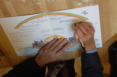 Rabbi Cantor Ron Broden's hands certify a baby naming certificate at a ceremony.