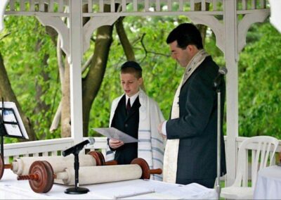 Rabbi Cantor Ron Broden officiates a Bar Mitzvah ceremony, with the Torah scroll open in front of him and a young boy reading from it.